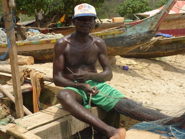 A fisherman repairs his nets after a large boat drove over them. (Butre, Ghana)